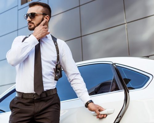 handsome-security-guard-listening-message-with-security-earpiece-on-street-and-opening-car